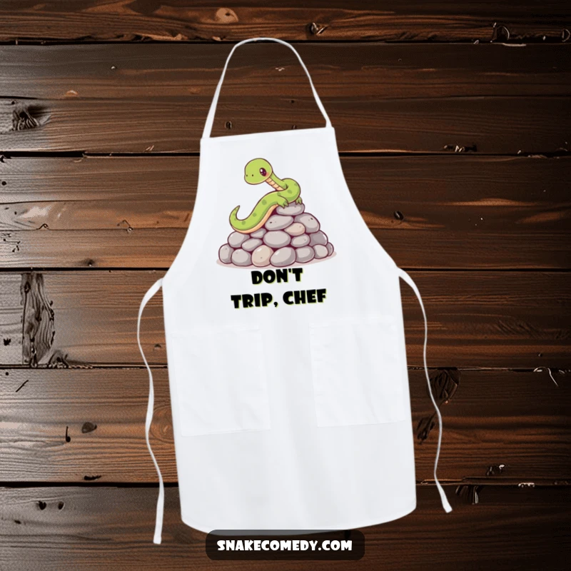 Funny apron featuring a cartoon snake comically slipping on a pile of smooth, round stones while attempting to cook or prepare food.