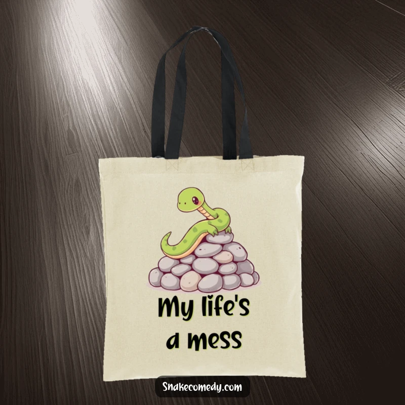 Funny tote bag illustrating a cartoon snake comically slipping and tumbling on a pile of smooth, round stones, full of surprise.